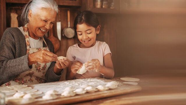 Grandmother and granddaughter making dumplings together in flour dusted kitchen background banner.