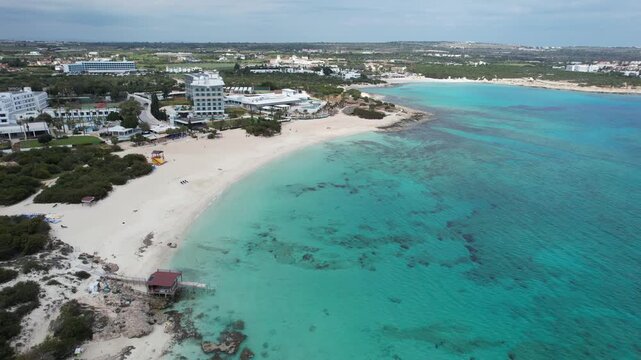 Drone 4k footage of curved sandy shoreline bordering crystal-clear turquoise waters and coastal holiday resort hotels. Makronissos bay beach Ayia Agia Napa Cyprus