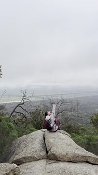 A girl hiker sits on a rock, admiring the beautiful view of the bush and plains at You Yangs Regional Park near Melbourne, Victoria, Australia.