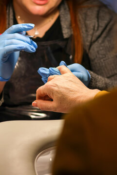 Nail technician wearing blue gloves performing a manicure procedure on a client's hand in a salon. Beauty, care, and hygiene concept