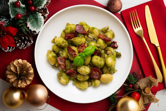 Delicious Italian gnocchi with pistachio pesto and fried bacon. Top-down view of the table. Christmas meal with a festively decorated table.