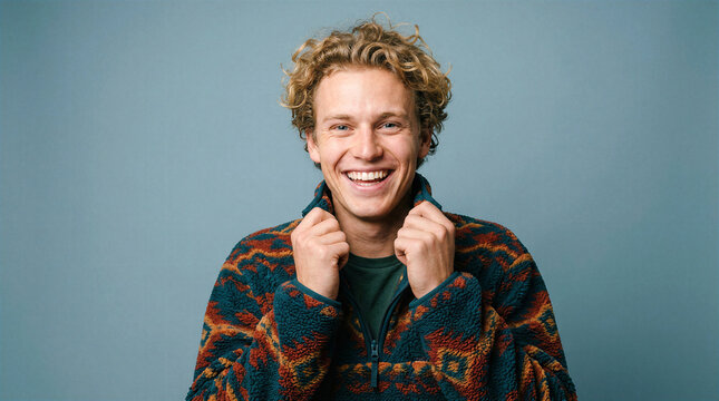 Young man with curly hair smiling broadly in a patterned fleece pullover