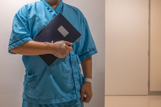 Hospital admission and medical insurance concept with patient in blue gown with iv catheter holding record file folder in clinic corridor for healthcare treatment and reimbursement claim.