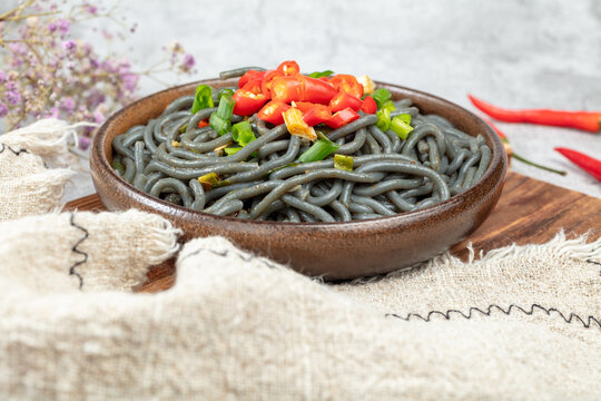 Dark Noodles with Tomatoes and Green Onions in a Rustic Bowl