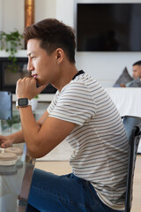 Obraz premium Diverse men sitting in living room, Asian man leaning on fist wearing smartwatch, headphones nearby