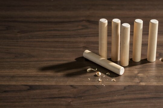 Row of pale wooden dowels standing on a walnut bench with fresh shavings