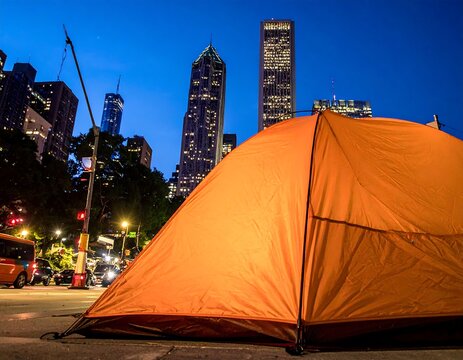 Bright orange camping tent set up on a sidewalk in a major metropolitan city at dusk. Ideal for illustrating urban homelessness and housing crises.