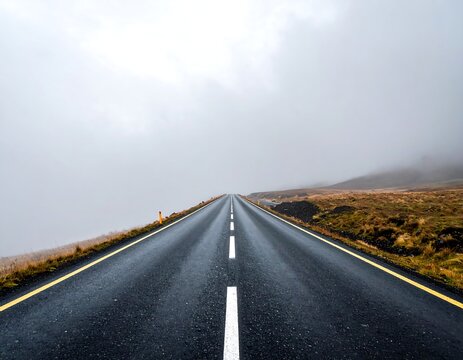 Straight asphalt road vanishing into a heavy foggy haze under an overcast sky. Ideal for travel and adventure concepts.
