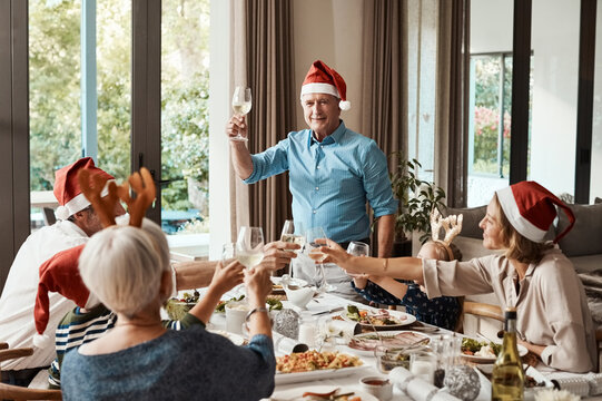 Grandpa, toast and Christmas lunch with family, celebration and festive with drinks in home. Grandparents, parents and children happy for holiday gathering, dinner party and cheers with beverage