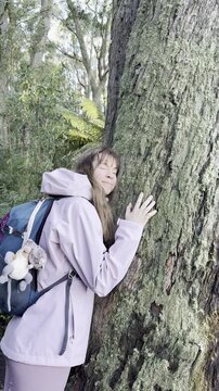 A girl hiker hugs the trunk of a large eucalyptus tree, connecting with nature along the trail to the summit of Mount Macedon near Melbourne, Victoria, Australia.
