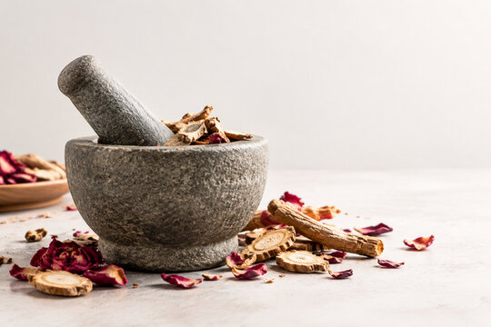Stone mortar and pestle with dried mandrake roots and petals, herbal apothecary still life