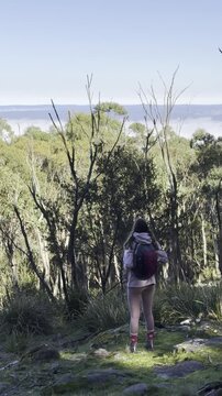 A girl hiker sits on rocks and admires the thick clouds emerging above the eucalyptus bush, from the summit of Mount Macedon, Macedon Ranges, near Melbourne, Victoria, Australia.