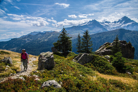 Hiker walking on a mountain trail in the Alps surrounded by green
