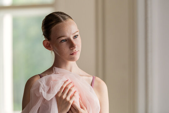 A young ballerina with freckles looks away thoughtfully