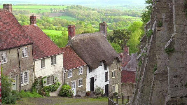 Charming english village houses nestled below medieval stone ruins in picturesque rolling landscape.