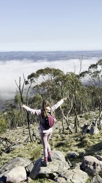 A girl hiker stands and admires the thick clouds emerging above the eucalyptus bush and a meadow, from the summit of Mount Macedon, Macedon Ranges, near Melbourne, Victoria, Australia
