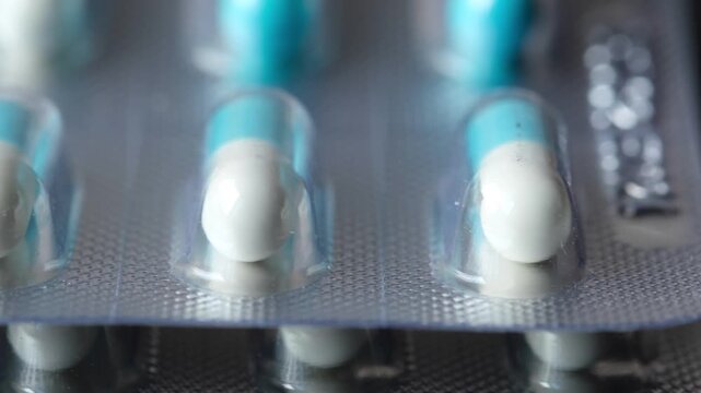 Macro view of blue and white medical capsules in transparent plastic blister packs on dark background