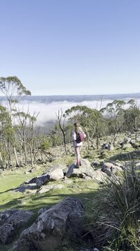 A girl hiker stands and admires the thick clouds emerging above the eucalyptus bush and a meadow, from the summit of Mount Macedon, Macedon Ranges, near Melbourne, Victoria, Australia