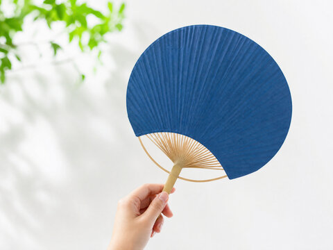 暑い夏の日に青いうちわを使って涼しい風をあおぐ手元