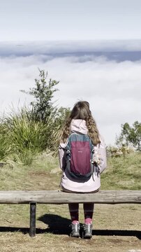 A girl hiker sits on the bench and admires the thick clouds emerging above the eucalyptus bush and a meadow, from the summit of Mount Macedon, Macedon Ranges, near Melbourne, Victoria, Australia
