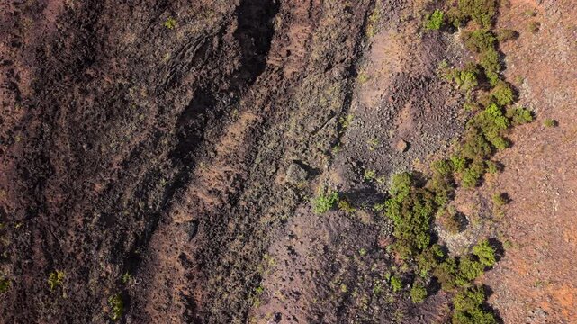 Aerial top down view of ancient volcanic lava flows on Maui Hawaii USA with dark basalt rock rust red cinder soil and patches of hardy green shrubs growing across the rugged crater slope.