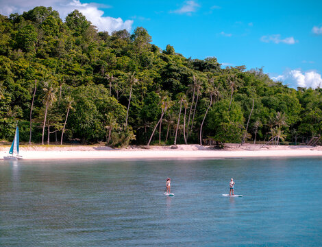 Top aerial view of couple of tourist are enjoy on water sport paddle sup-board with kayaking along at the edge of the sea beach under crystal clear of water in the island of summer trip