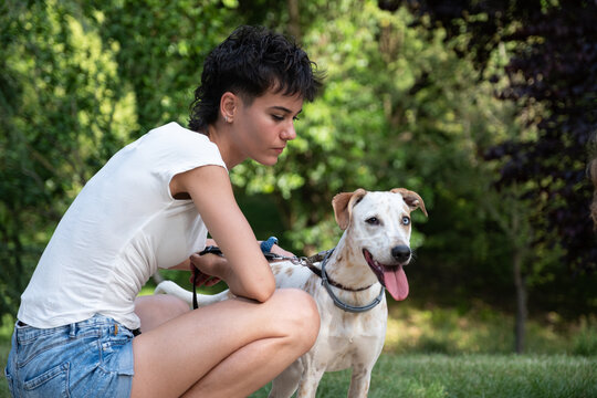 Young woman with short hair interacting with her dog on leash outdoors