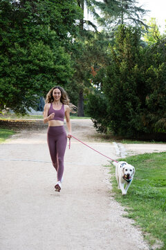 Woman running for fitness with her dog on a leash in a green park