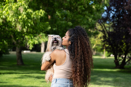 Woman embracing and kissing a happy shih tzu dog outdoors, expressing love and friendship