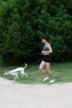 Woman running outdoors with her dog on a leash, exercising in nature