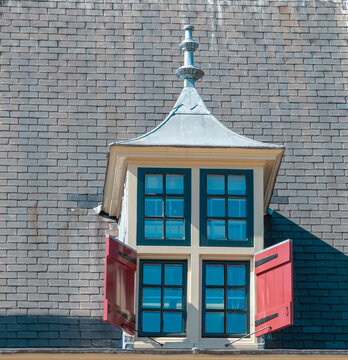 Vintage dormer window with open red shutters on roof A detailed shot of a classic architectural dormer window featuring green framed glass panes, open red wooden shutters
