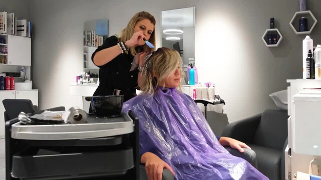 Woman client getting hair colored by female hairdresser in beauty salon. Styling and customer service in parlor.