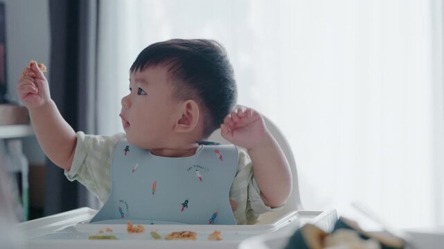 Asian toddler eating breakfast in high chair, baby-led weaning BLW concept