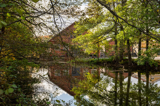 Old brick building reflected in calm water surrounded by green autumn trees in Finland