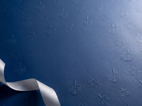 Navy blue textured paper with embossed dreidel Star of David pattern and silver ribbon creating elegant background for holiday. Hanukkah or Chanukah Jewish celebration concept with copy space.