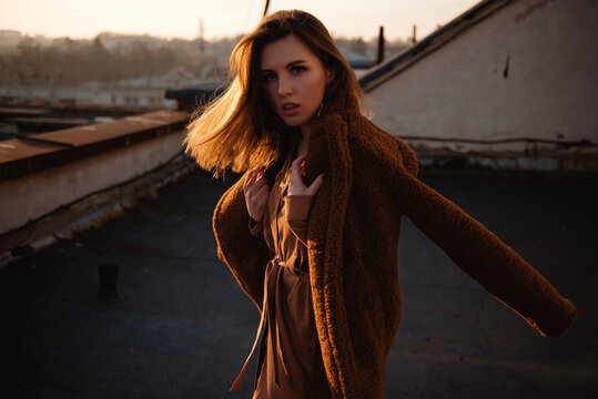 Young woman in a cozy teddy coat on a rooftop at sunset