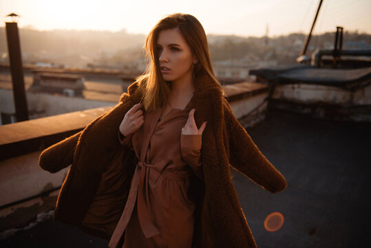 Woman in warm coat on rooftop during golden hour sunset