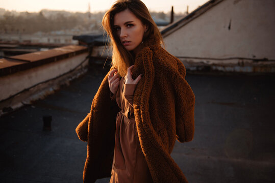 Young woman in a cozy teddy coat on a rooftop at sunset