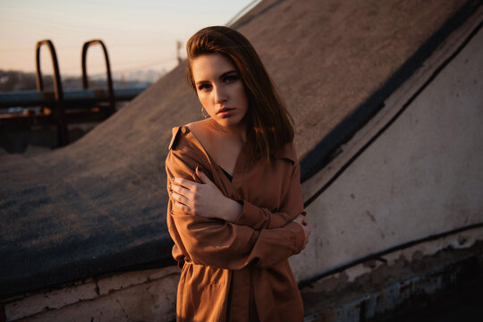 Young woman in stylish outfit posing on a rooftop at sunset