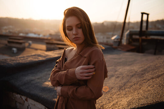 Woman in brown shirt posing on rooftop during golden hour sunset