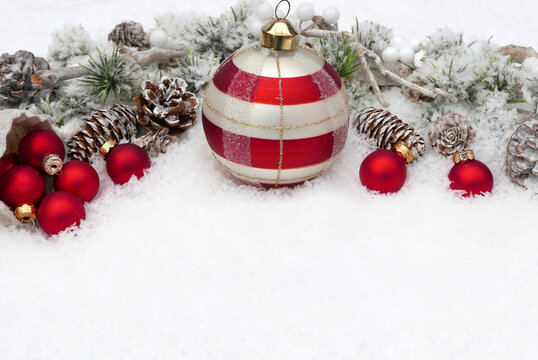 Festive Christmas background with red and white Christmas baubles, pine cones, and snow-covered branches in the snow, with space for text.
