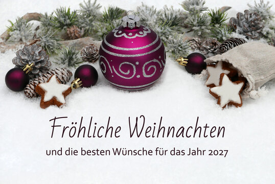Weihnachtskarte:  Dekoration mit Tannenzweigen, Zapfen, Zimtsternen und einer gro&szlig;en lila Christbaumkugel auf Schnee mit dem Text 'Fr&ouml;hliche Weihnachten und die besten W&uuml;nsche f&uuml;r das Jahr 2027'