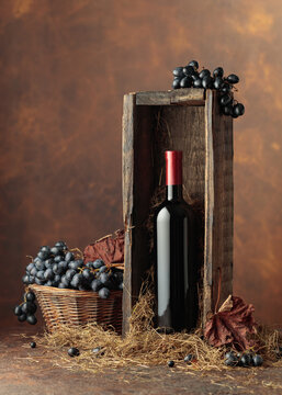 Bottle of red wine in old wooden box and blue grapes in basket.