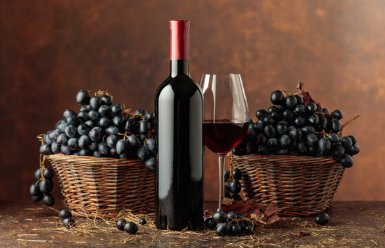 Bottle of red wine and blue grapes in old basket.