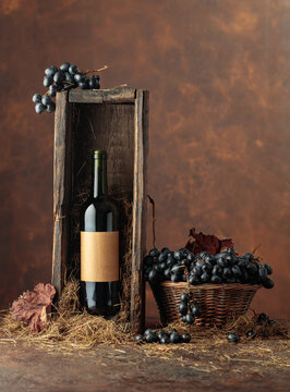 Bottle of red wine in old wooden box and blue grapes in basket.