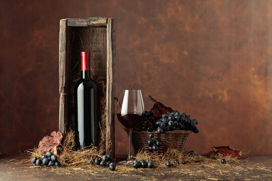 Bottle of red wine in old wooden box and blue grapes in basket.
