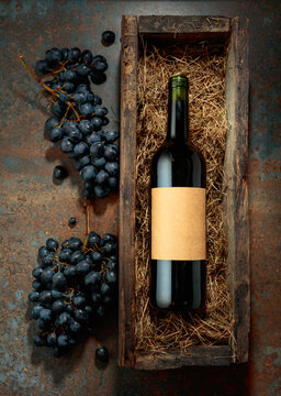 Bottle of red wine in an antique wooden box and fresh grapes.