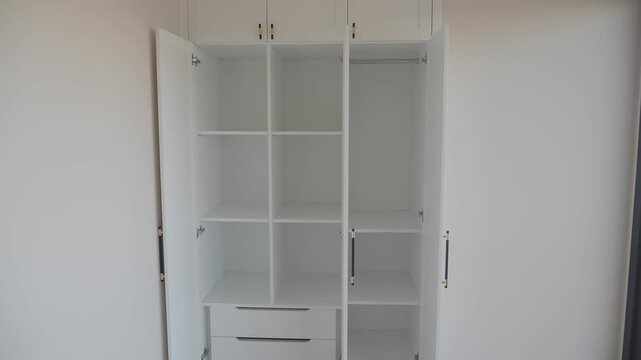 Clean empty white wardrobe with open doors and drawers reveals organized storage space in bright room
