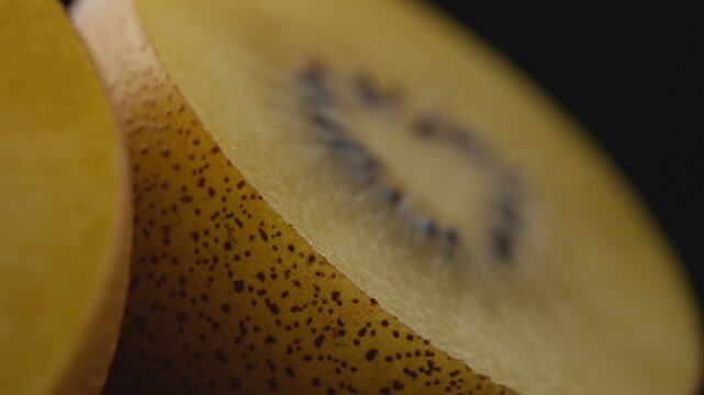 Extreme macro shot of a halved ripe golden kiwi with selective focus on the smooth peel, showing juicy pulp and seeds in the background for healthy eating, gourmet food, and culinary concepts.