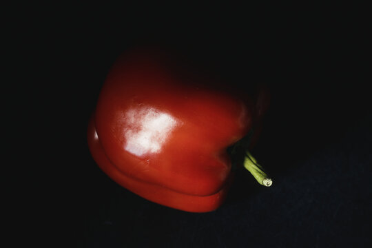 Close-up of ripe red bell pepper with vibrant green stem in moody lighting on dark background. Fresh raw vegetable for organic recipes, culinary menus, nutrition, and healthy eating.